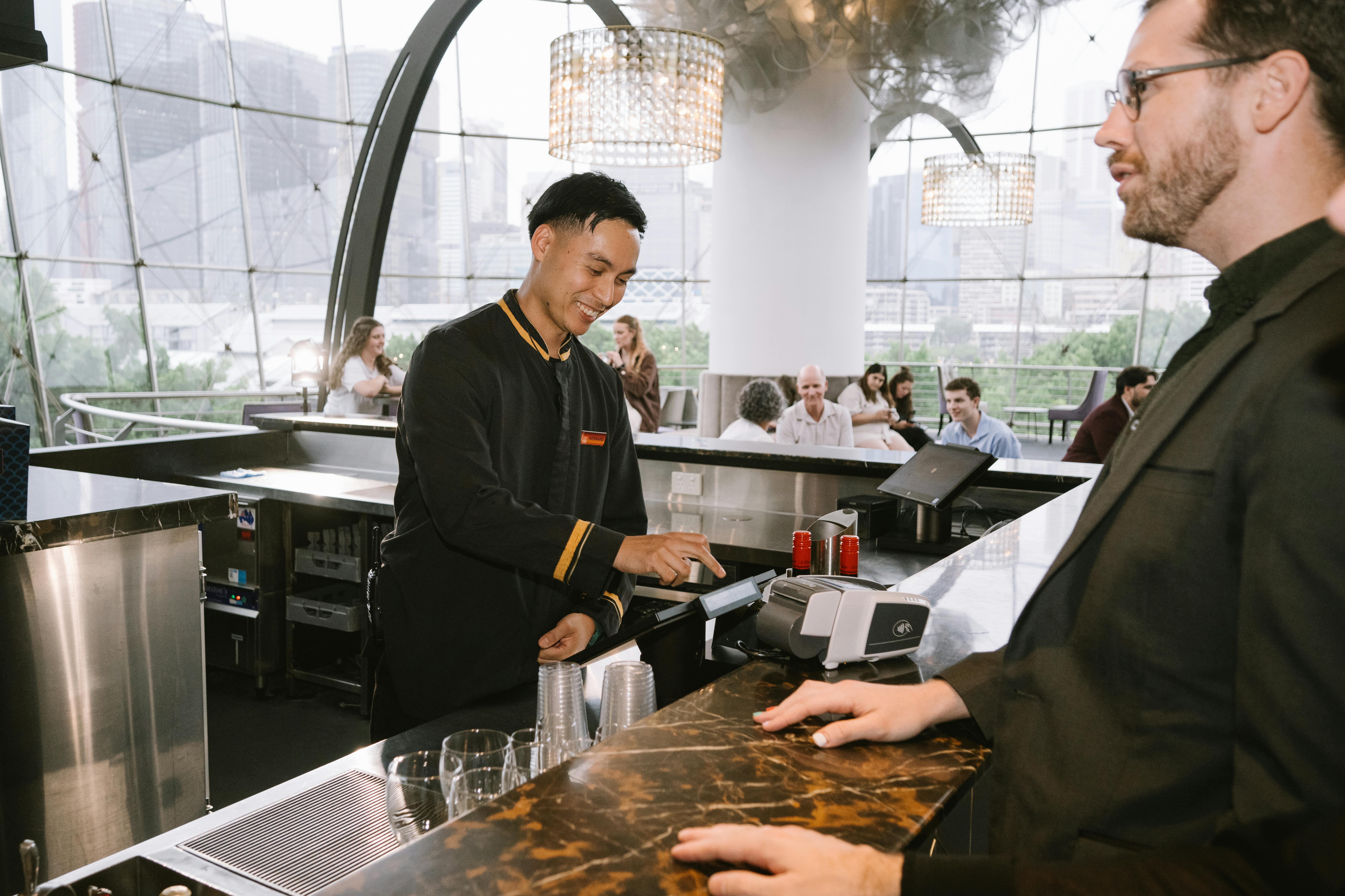 A bar attendant stands behind the bar at the Sydney Lyric. They are serving a customer.